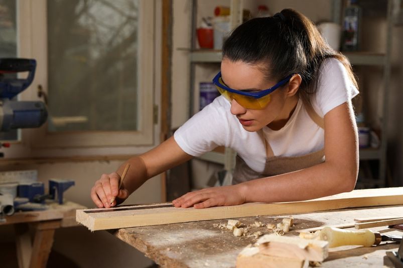 mujer con gafas de proteccion midiendo tabla madera